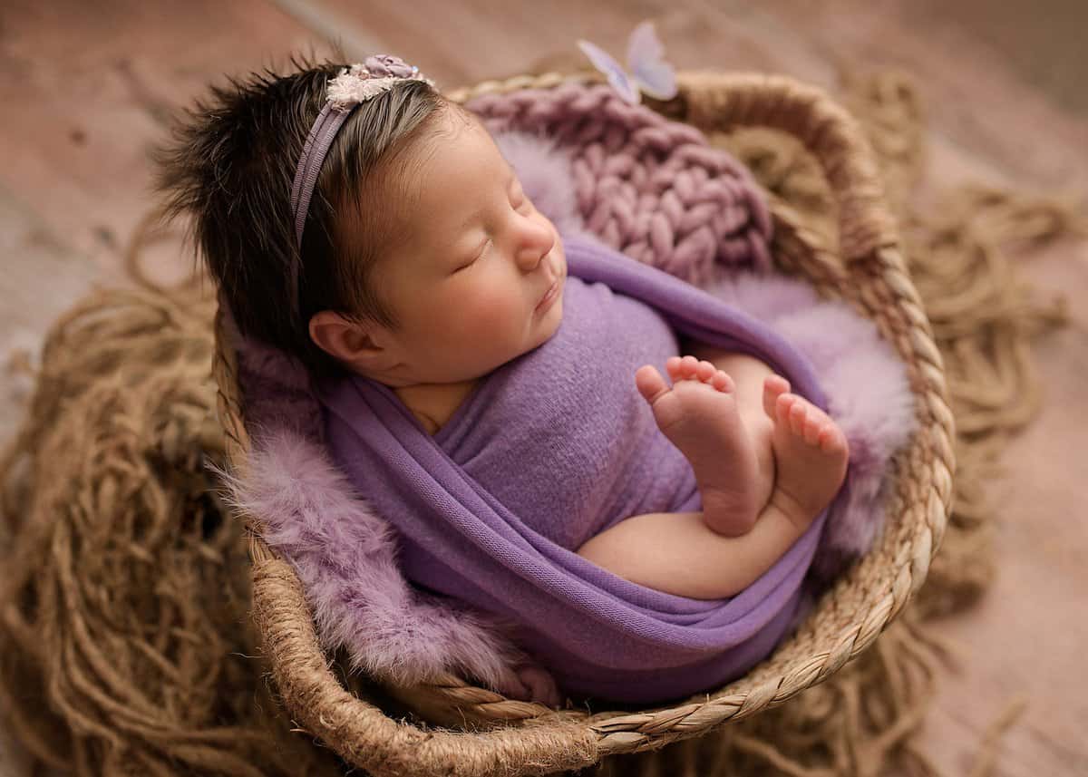 newborn babygirl photographed professionally in a basket wearing purple, newborn photography atlanta ga, hiram newborn session, newborn portraits atlanta, baby photographer atlanta, posed newborn photographer near me, posed newborn photoshoot atlanta, douglasville studio photographer