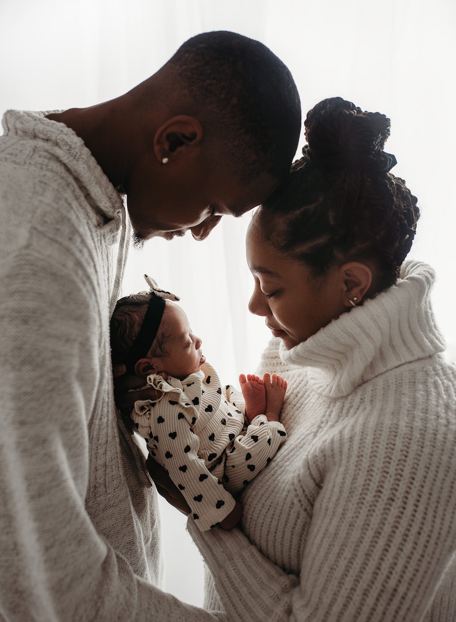 mom and dad touching heads holding their newborn baby during a newborn photoshoot in atlanta