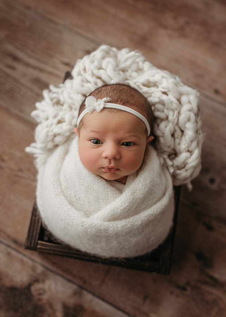 newborn baby girl photographed using neutral colors, newborn tieback, newborn eyes open photos, newborn wrapped in box prop