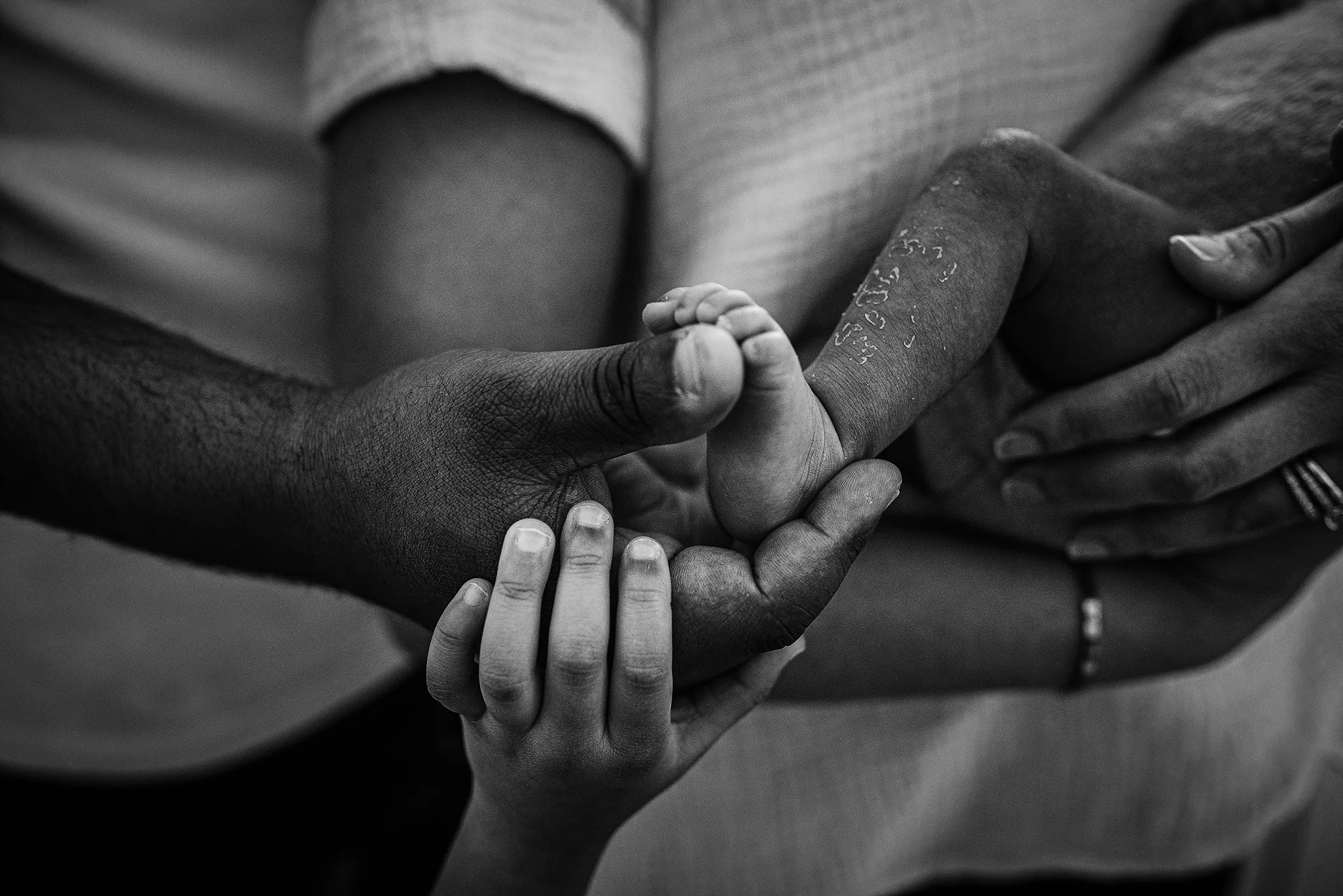 black and white photo of newborn photography details of mom, dad, big sisters hands with a tiny newborn foot