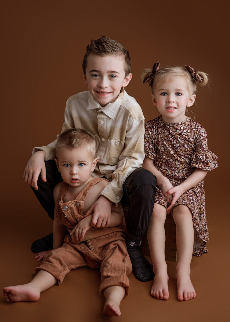 siblings posed on brown backdrop for studio family session, lincoln family photographer, family photoshoot nebraska, omaha family photographer