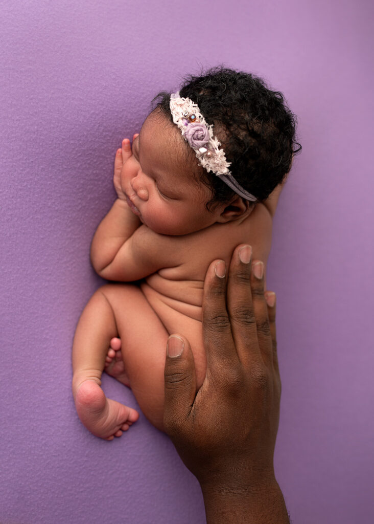 newborn girl posed with dads hand to show how tiny she once was, newborn details, purple newborn set up ideas, purple tieback, newborn photo session near me