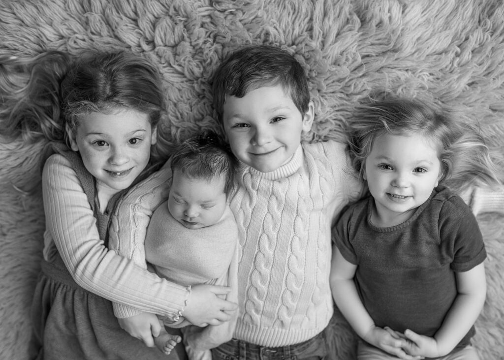 siblings posed with new baby brother during newborn photography session, photographer with props in lincoln ne, lincoln nebraska newborn photoshoot