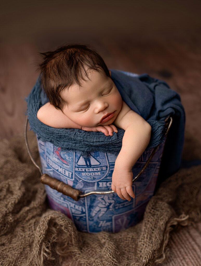 baby posed in hello little props hockey bucket during newborn photo session in nebraska, lincoln nebraska newborn photos, photographer with props in lincoln, studio rental lincoln nebraska