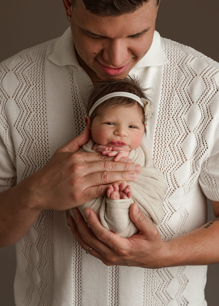 awake baby girl with floral headband in dads hands captured by Indiana newborn photographer