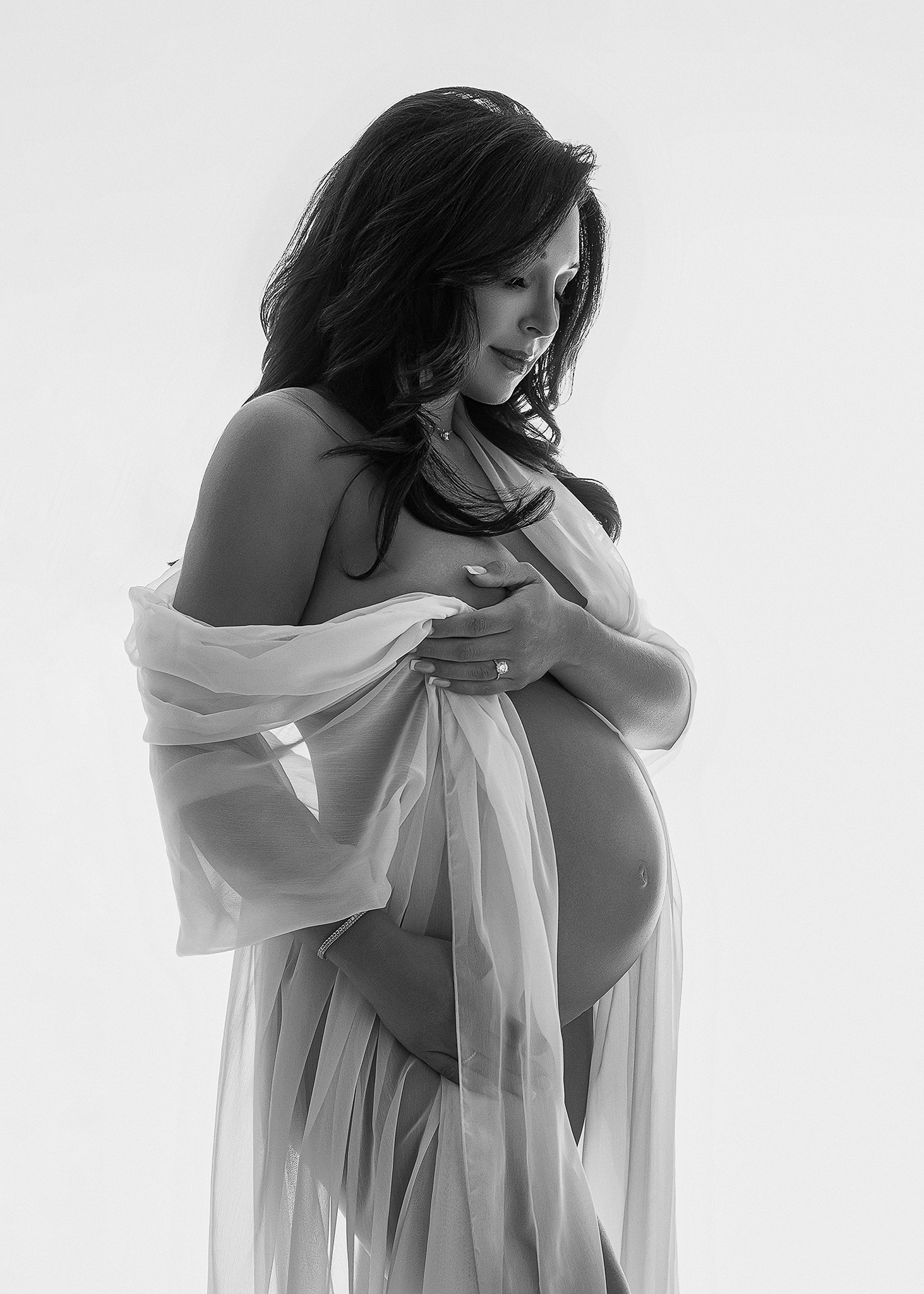 mom to be photographed in black and white with a sheer drape during maternity portrait session in west lafayette Indiana