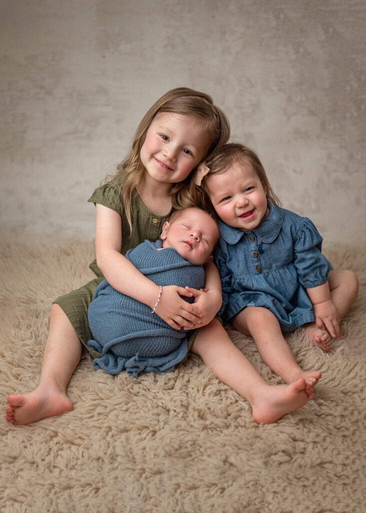 sweet sisters snuggling their new baby brother in their in-home studio experience with lafayette photographer