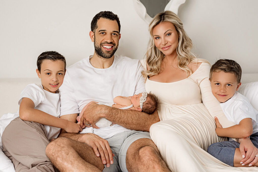 Family of 5 posed on their bed for a polished luxury newborn session in indiana