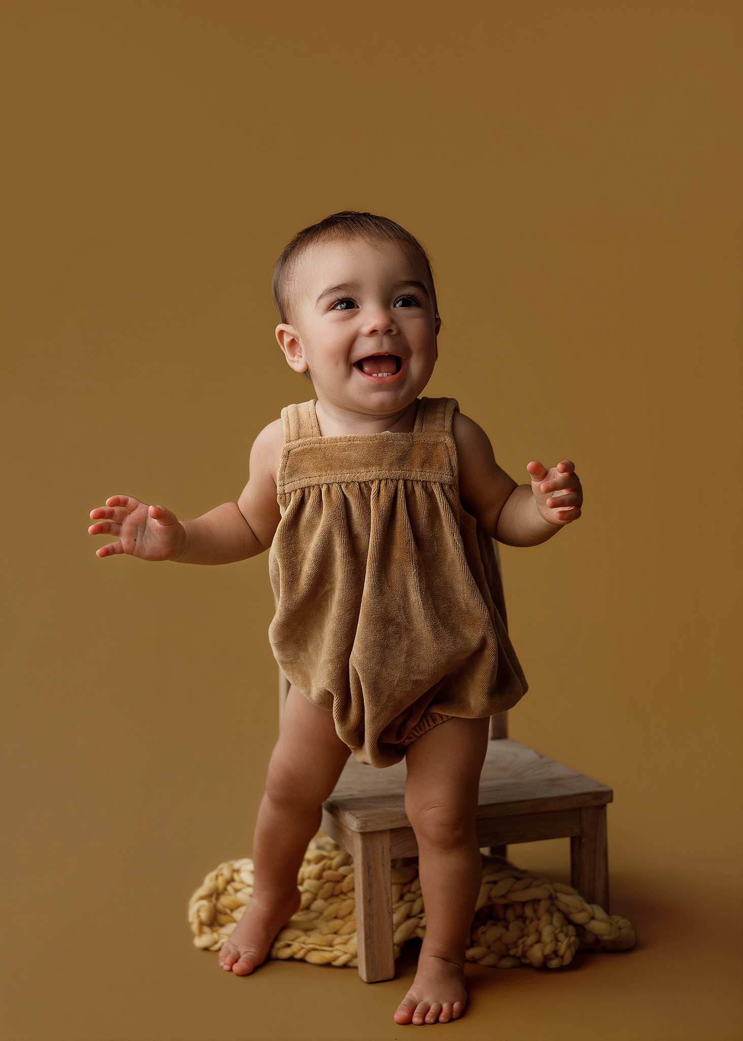 First birthday milestone portrait of a one-year-old in mustard yellow with a professional studio setup brought to the family's home